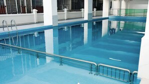 Une piscine intérieure à l’eau claire, dotée de rampes en métal et d’un revêtement de sol carrelé.