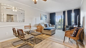 A modern living room with a glass dining table, wicker chairs, a sofa, and a ceiling fan.