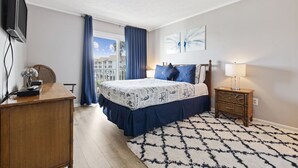 A bedroom with a bed, a television, a desk, and a window with curtains.