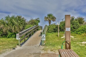 Une promenade en bois mène à une zone de plage où des panneaux indiquent qu’il est interdit d’y amener des animaux et mettent en garde contre l’interruption de la fourniture d’eau.