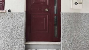 Une porte de couleur bordeaux ornée d’un heurtoir en laiton, une petite fenêtre avec un panneau en verre dépoli et une boîte aux lettres blanche portant un symbole noir.