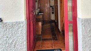 Un couloir étroit avec un plafond en bois et une porte rouge sur le côté gauche. Un panneau bleu avec les lettres « AL » est visible sur le mur.