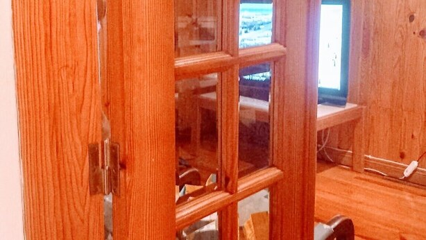 Une porte en bois avec un panneau de verre, qui donne sur une pièce contenant un ordinateur et une chaise.