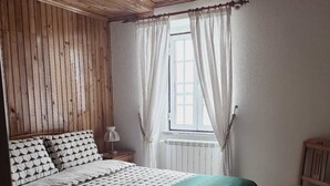 Une pièce aux murs lambrissés, avec un lit, une chaise et une fenêtre ornée de rideaux.