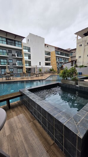 A modern outdoor pool area with a hot tub, surrounded by lounge chairs and umbrellas. - Piscina Privativa 03c Bela Vista by LP (Ipojuca)