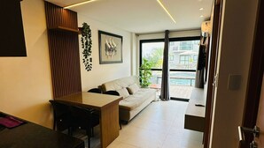 Un salon moderne comprenant un canapé, une table basse et un coin repas avec une table et des chaises. Une grande fenêtre offre une vue sur l’extérieur.
