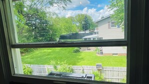 A window with a view of a backyard, including a wooden fence, a lawn, and a house. - Spacious 3BR Home w/ 8 Beds, Big Yard & Parking – Near Canton & Hall of Fame (Massillon)