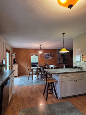 A kitchen with wooden walls, a dining area with chairs, a central island, and a hanging light fixture.