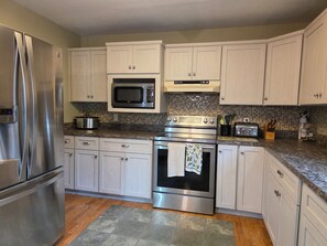 A kitchen with stainless steel appliances, white cabinets, a microwave, a toaster, and a tiled backsplash.