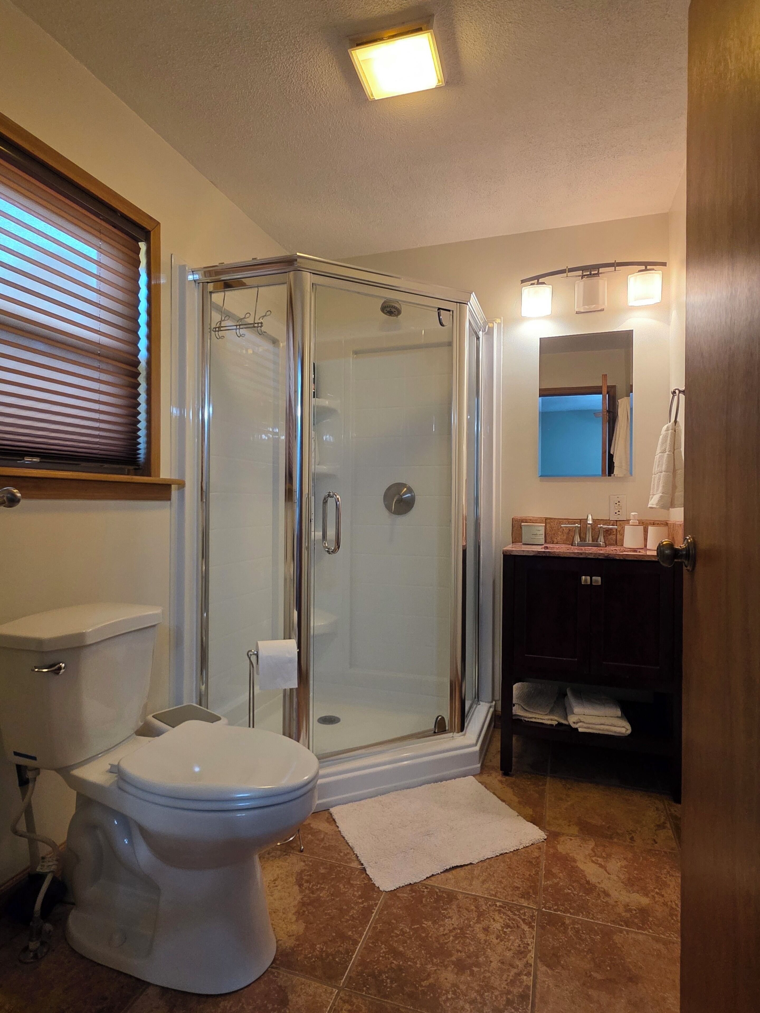 Un baño con ducha de vidrio, inodoro, lavabo con tocador y espejo.