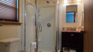 Un baño con ducha de vidrio, inodoro, lavabo con tocador y espejo.
