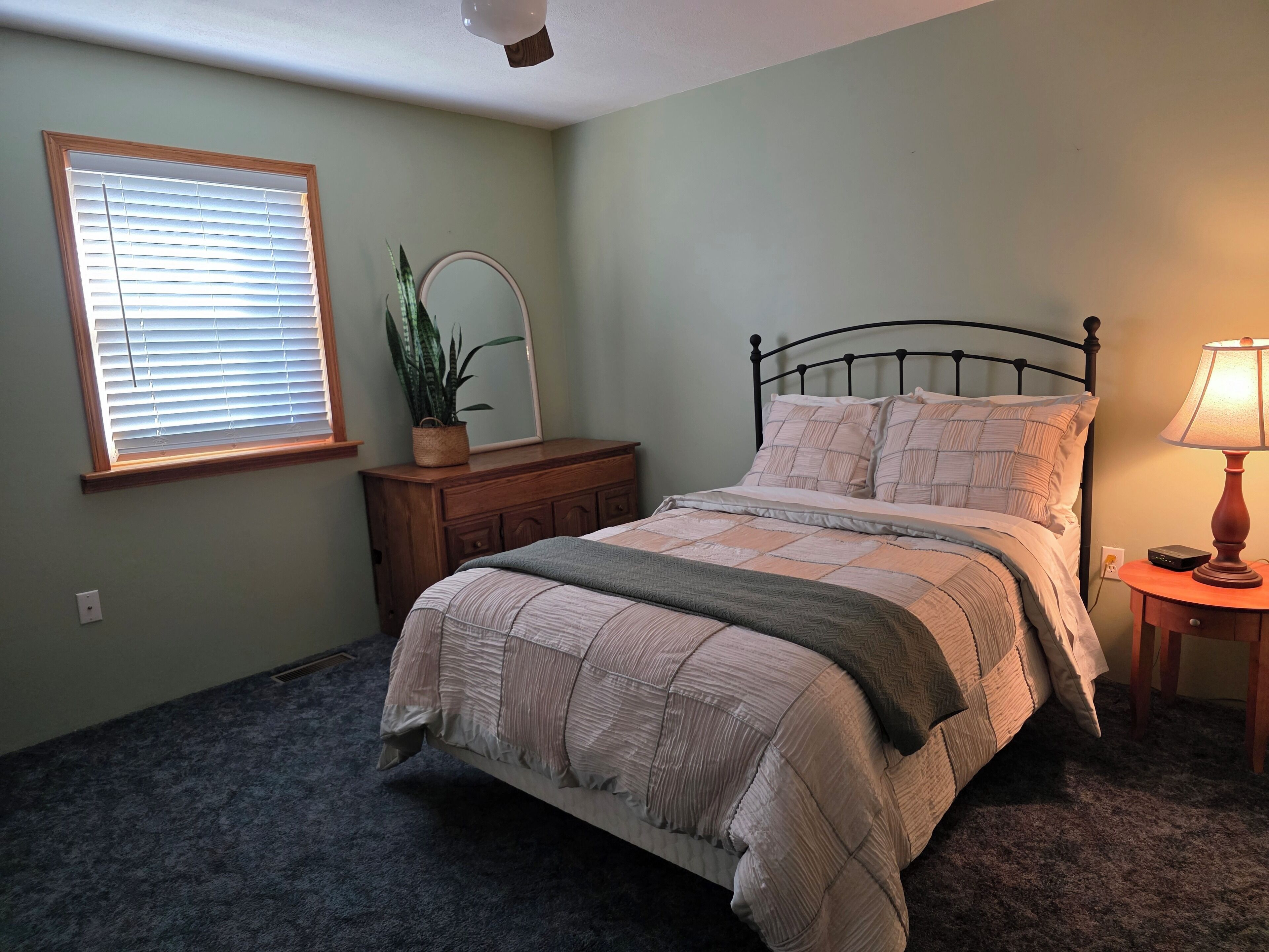 Ein Schlafzimmer mit Bett, Kommode, Spiegel und Nachttischlampe.