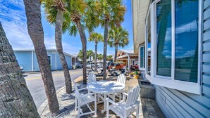 A patio with white chairs and a table, palm trees, a building with large windows, and a parked golf cart.