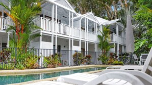 A white building with balconies, a pool, and lounge chairs.