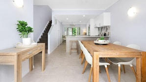 A modern kitchen with a wooden dining table, white chairs, and a staircase leading to another level.