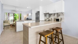 A modern kitchen with white cabinets, a large island, and two wooden stools.