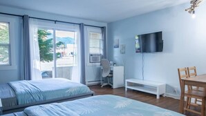 A hotel room with two beds, a desk, a chair, a TV, and a window with curtains. - The Driftwalk | Walkable to Beach (Harrison Hot Springs)