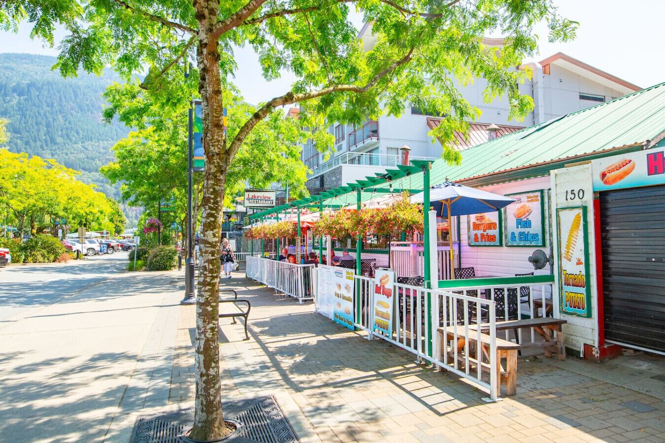 A street with outdoor food stalls, a restaurant, and a mountain in the background.