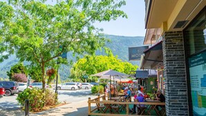 A restaurant with outdoor seating, cars parked in the background, and a mountain view. - The Driftwalk | Walkable to Beach (Harrison Hot Springs)
