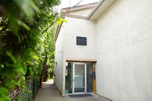 Un sendero estrecho que conduce a un edificio con puerta de vidrio y un letrero arriba.