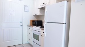 Une cuisine de taille réduite avec des meubles blancs, un réfrigérateur blanc, un four à micro-ondes et une cuisinière.