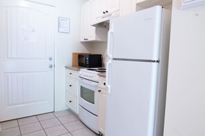 A compact kitchen with white cabinetry, a white refrigerator, a microwave, and a stove.
