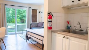 Une chambre avec un lit, une fenêtre avec des rideaux, une table de chevet et une chaise. La chambre est dotée d’une porte-fenêtre coulissante qui donne sur un balcon.