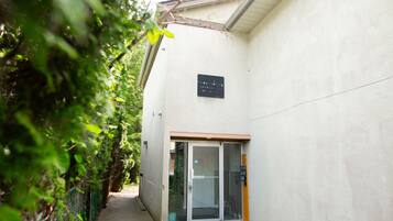 Un étroit sentier mène à un bâtiment dont l’entrée est une porte en verre, et une enseigne est placée au-dessus.