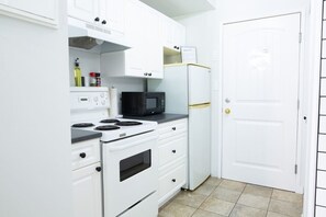 A compact kitchen with white cabinetry, a stove, a microwave, and a refrigerator.
