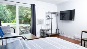 Une chambre moderne comprenant un lit, un bureau, une chaise, une télévision et un balcon avec vue sur la verdure.