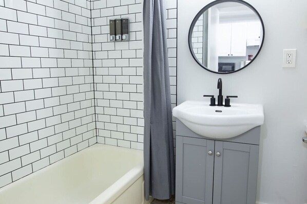 Un baño con paredes de azulejos blancos, un lavamanos blanco y una bañera.
