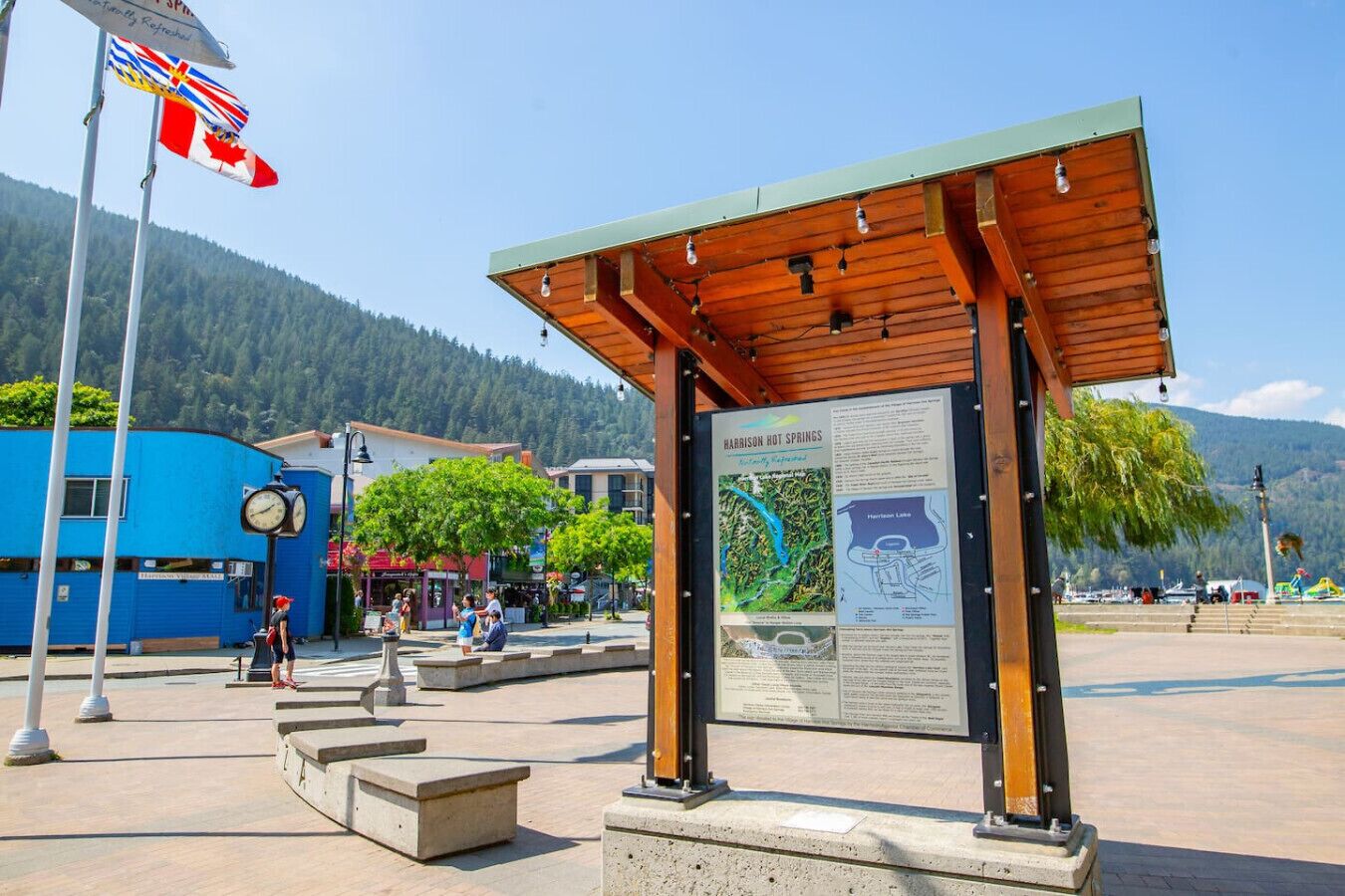 A wooden pavilion with a signboard, a clock, and a flagpole with flags.