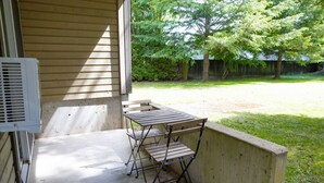 A patio with a table and chairs, a vent on the wall, and a view of a yard with trees. - The Backyard @ Cedar Springs | Walk to Lake & Hot Springs (Harrison Hot Springs)
