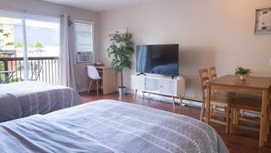 A hotel room with two beds, a TV, a desk, and a dining table. - Beachy 2 Bed Studio Suite, Balcony and 4 Min to Lake (Harrison Hot Springs)