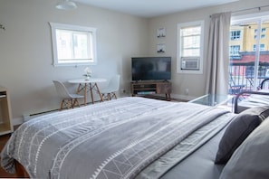 Une chambre avec un grand lit, une télévision, une petite table avec des chaises et un balcon donnant sur des immeubles.