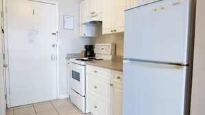 Een kleine keuken met witte kastjes, een kookplaat, een oven en een koelkast.