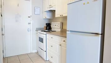 A compact kitchen with white cabinetry, a stove, an oven, and a refrigerator.