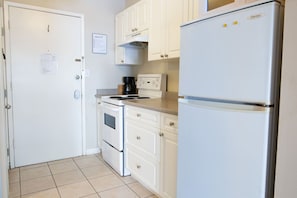 Une cuisine de taille réduite, dotée de meubles blancs, d’une cuisinière, d’un four et d’un réfrigérateur.