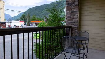 A balcony with a metal railing, two metal chairs, and a view of a street with buildings and a mountain in the background.