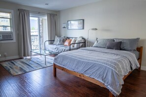 A bedroom with a large bed, a smaller bed, a chair, a lamp, and a window with curtains.