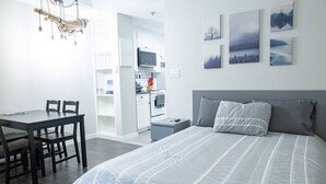 A modern bedroom with a large bed, a dining table with chairs, and a kitchenette.