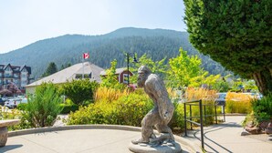 A stone sculpture of a bear in a park with a mountain backdrop and buildings in the distance.