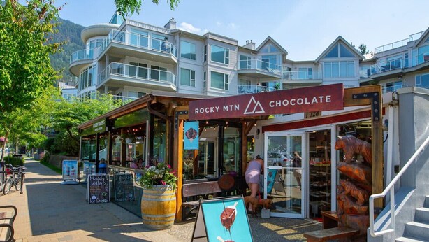 A Rocky Mountain Chocolate store with a signboard, a large chocolate sculpture, and a view of a mountain in the background.