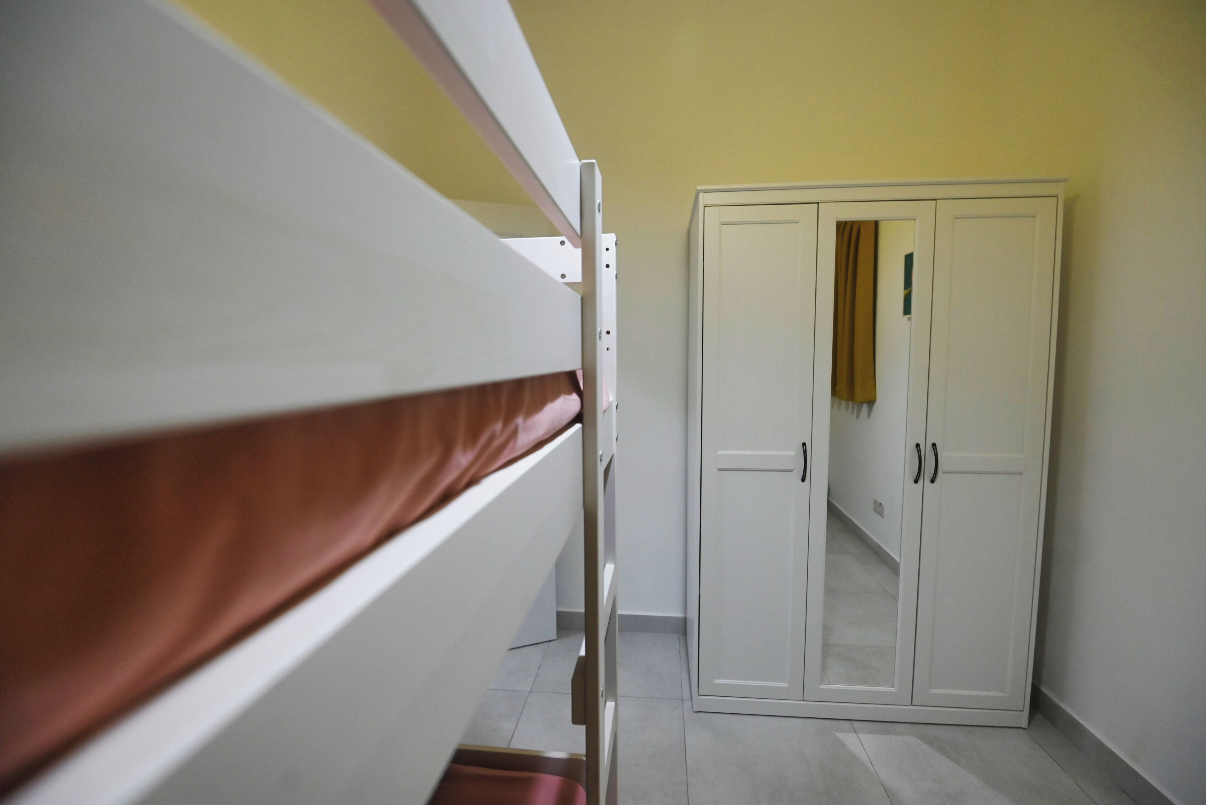 A bunk bed with a brown mattress, a white wardrobe with two doors, and a yellow wall.