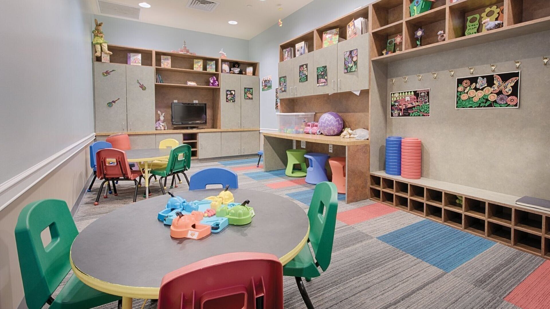 A children's playroom with colorful chairs, a round table, and shelves with toys and books.