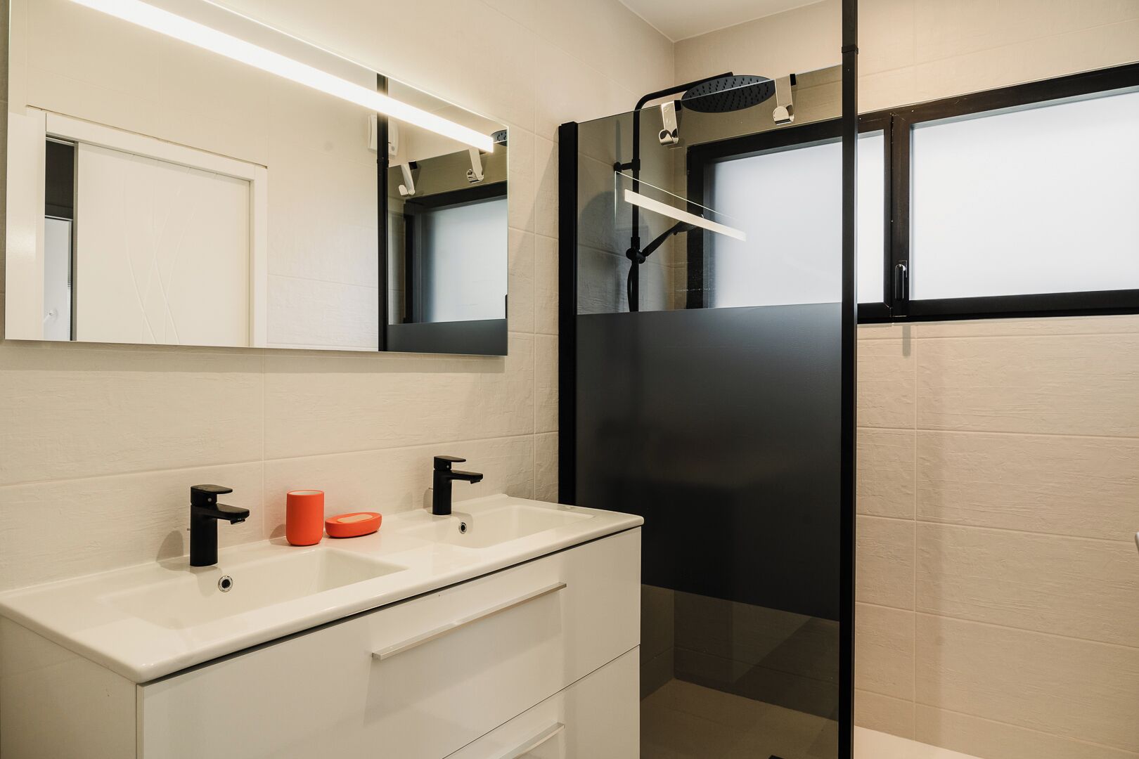 A modern bathroom with a white vanity, black faucets, and a glass shower enclosure.