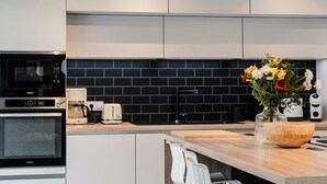 A modern kitchen with a black tiled backsplash, a built-in microwave, a coffee maker, and a toaster. - Modern villa with Spa 10 pers (santec)