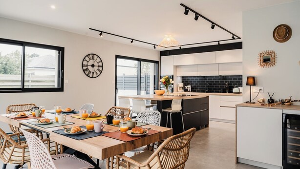 A modern kitchen with a dining area, featuring a large island, black and white cabinetry, and a breakfast setup with croissants and orange juice. - Modern villa with Spa 10 pers (santec)