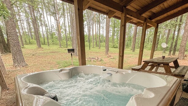 A hot tub under a wooden pavilion with a forest view. - Luxury cabin getaway on a 40 acre retreat (Bismarck)