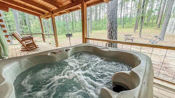 Un bain à remous avec une terrasse en bois et une vue sur une forêt.